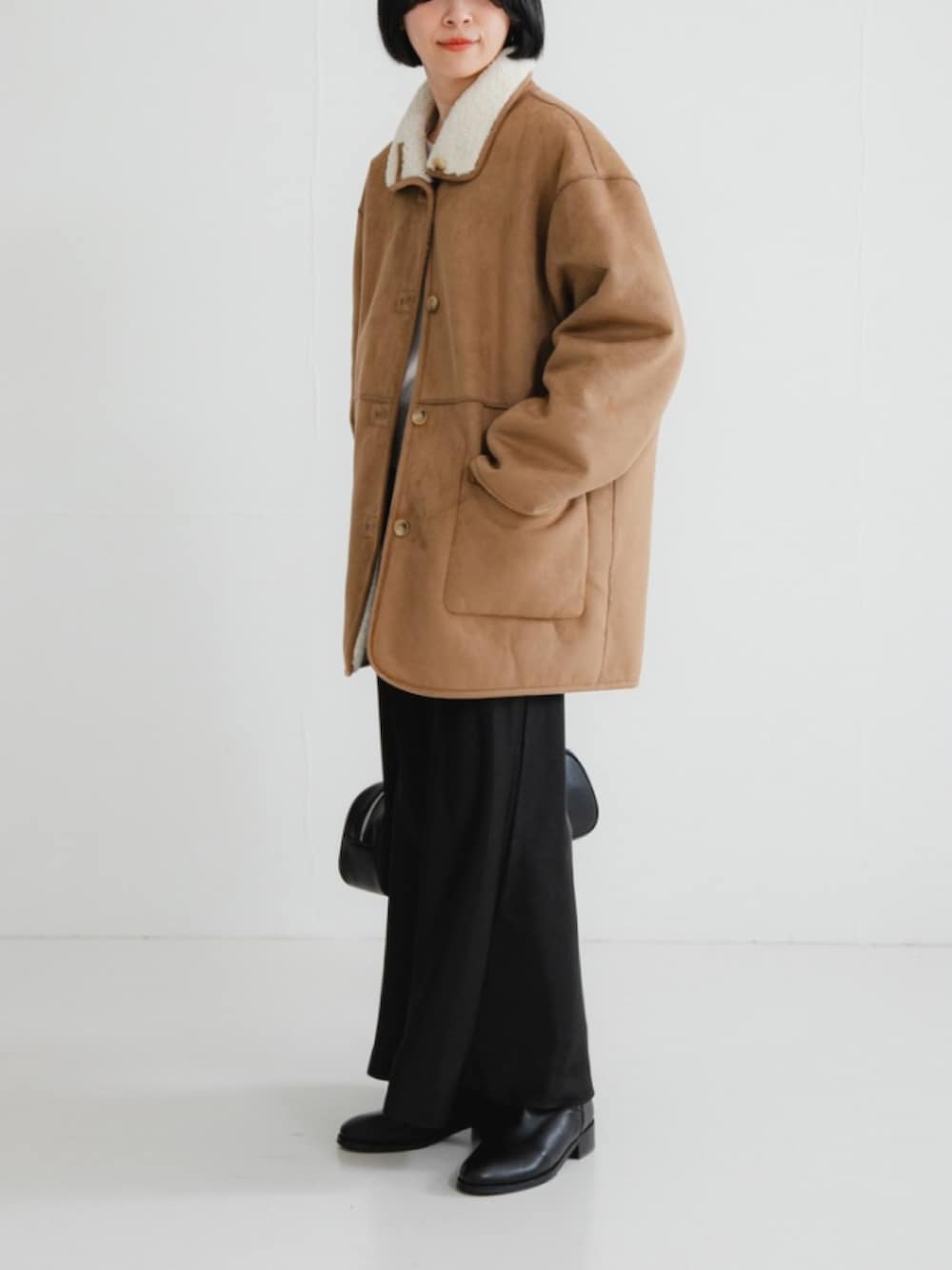 ホワイト系のムートンコート、グレー系のニット/セーター、ブラック系のスカートを着用したレディースの冬コーディネートの2枚目の写真