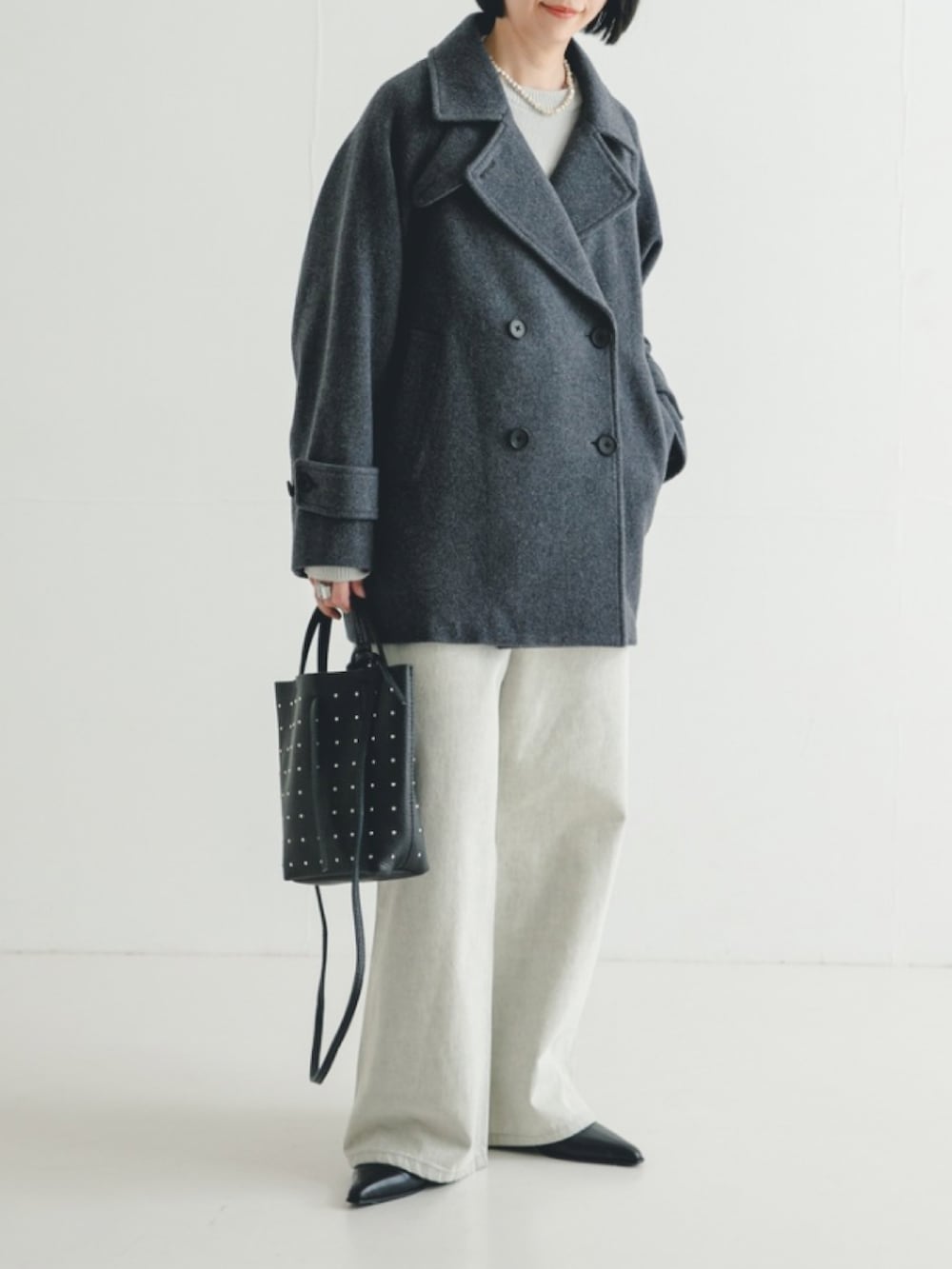 ブラック系のトートバッグ、グレー系のデニムパンツ、グレー系のピーコートを着用したレディースの冬コーディネートの2枚目の写真