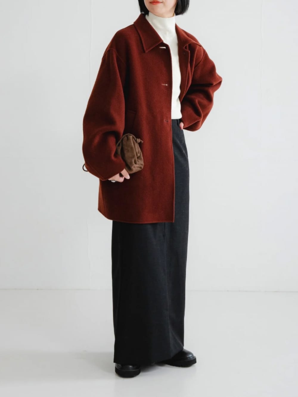 ブラウン系のステンカラーコート、ホワイト系のニット/セーター、ブラック系のスカートを着用したレディースの冬コーディネートの2枚目の写真