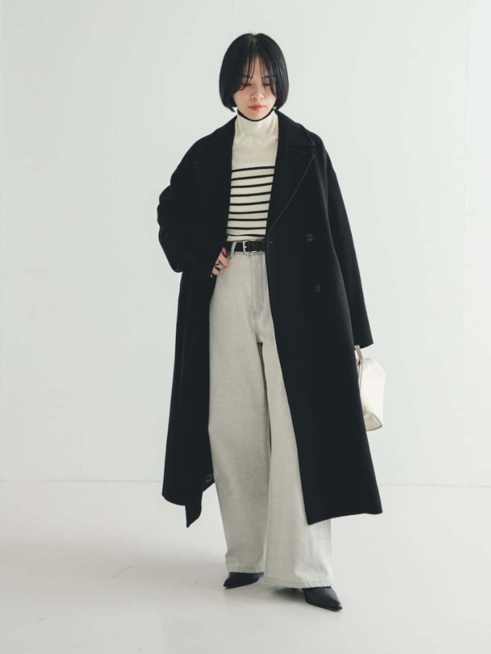 ブラック系のチェスターコート、ホワイト系のニット/セーター、グレー系のデニムパンツを着用したレディースの冬コーディネートの3枚目の写真