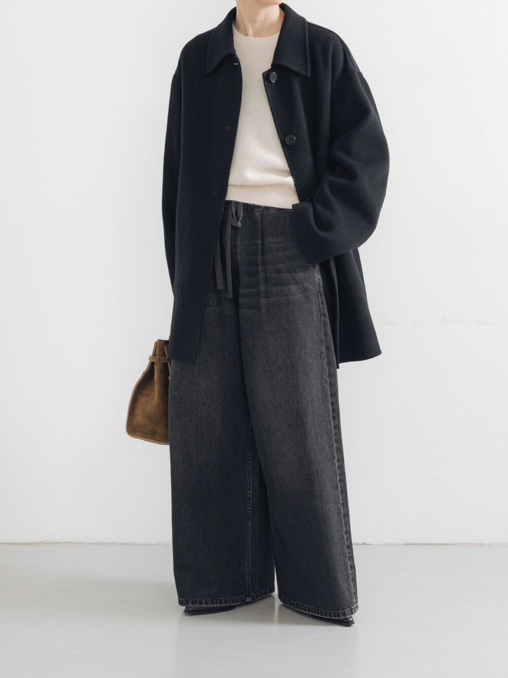 ホワイト系のベスト、ブラック系のステンカラーコート、ブラック系のデニムパンツを着用したレディースの秋コーディネートの3枚目の写真