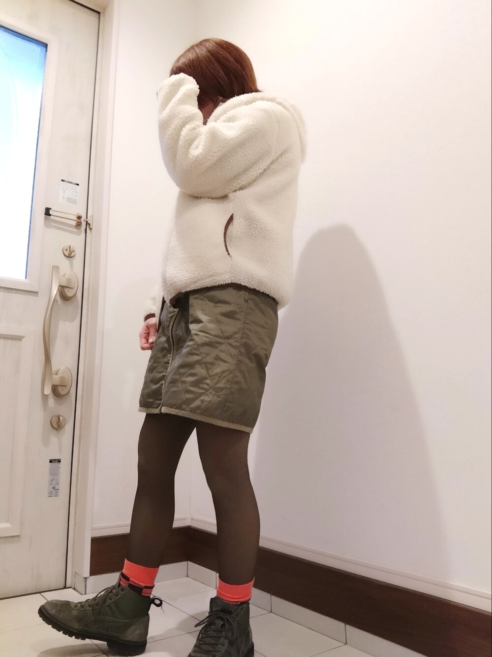 グリーン系のスカート、オレンジ系のスウェット、ブラウン系のマウンテンパーカーを着用したレディースの冬コーディネートの2枚目の写真