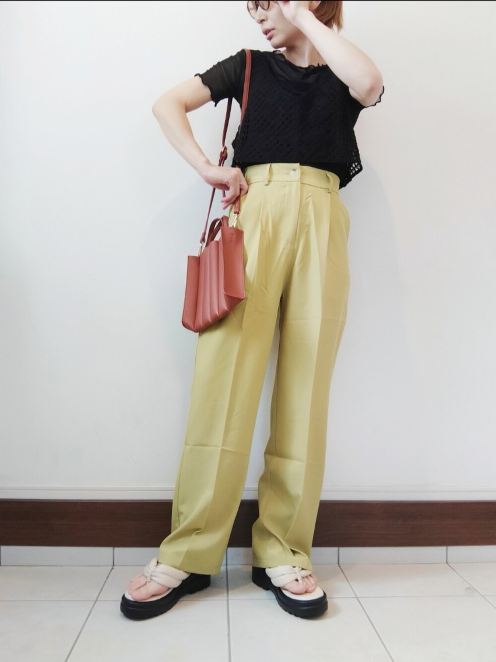 ブラック系のベスト、ベージュ系のトートバッグ、イエロー系のスラックスを着用したレディースの夏コーディネートの2枚目の写真