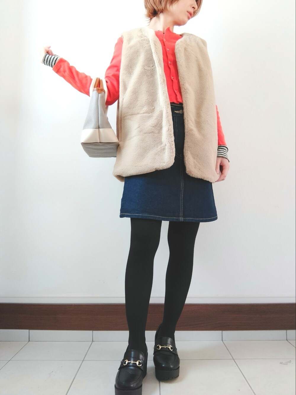 ベージュ系のベスト、オレンジ系のカーディガン/ボレロ、ブルー系のデニムスカートを着用したレディースの冬コーディネートの2枚目の写真