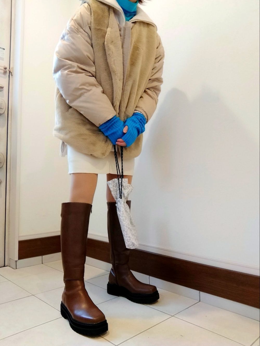 ベージュ系のダウンジャケット/コート、オレンジ系のニット/セーター、ホワイト系のスカートを着用したレディースの冬コーディネートの2枚目の写真