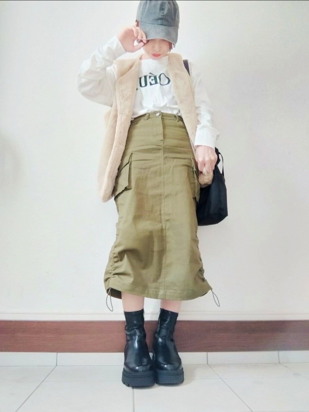 ベージュ系のベスト、ブラック系のショルダーバッグ、グリーン系のスカートを着用したレディースの秋コーディネートの2枚目の写真