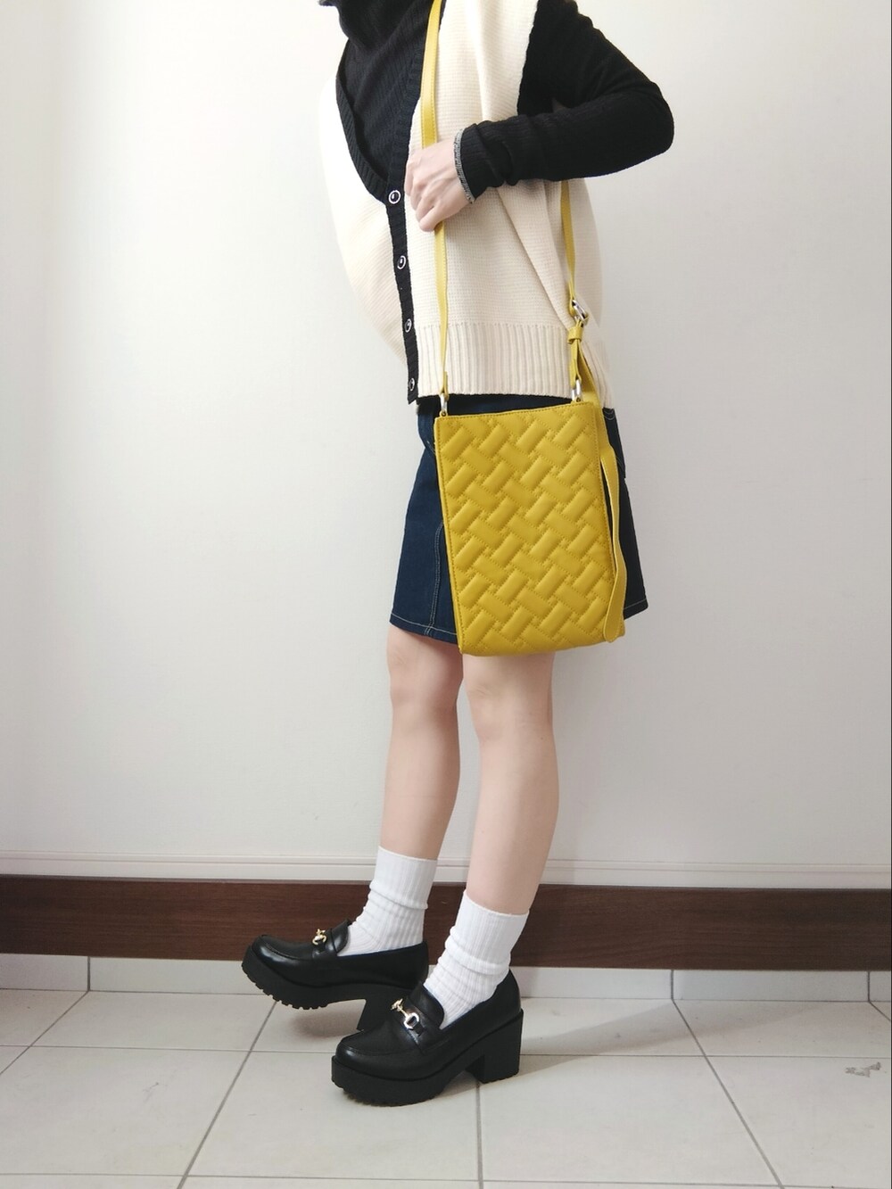 ホワイト系のベスト、イエロー系のショルダーバッグ、ブルー系のデニムスカートを着用したレディースの春コーディネートの2枚目の写真