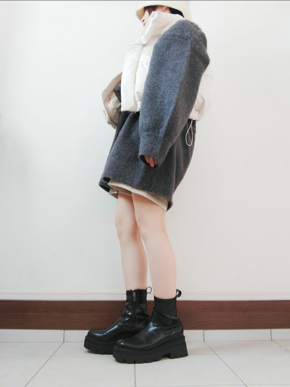 ホワイト系のダウンベスト、グレー系のカーディガン/ボレロ、ブラック系のブーツを着用したレディースの冬コーディネートの2枚目の写真