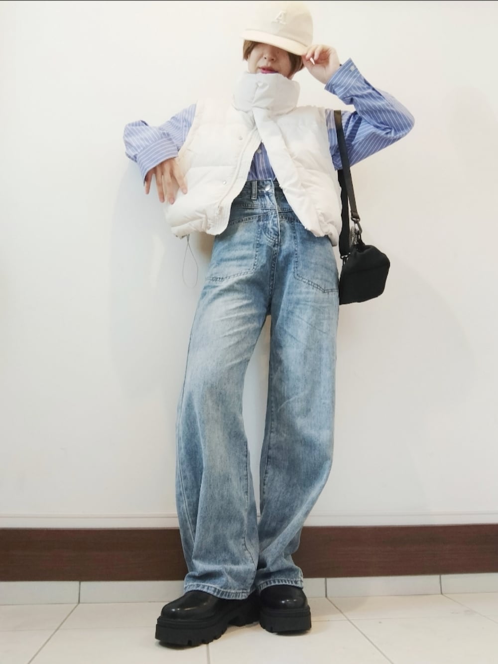 ホワイト系のダウンベスト、ブラック系のショルダーバッグ、ブルー系のデニムパンツを着用したレディースの秋コーディネートの2枚目の写真