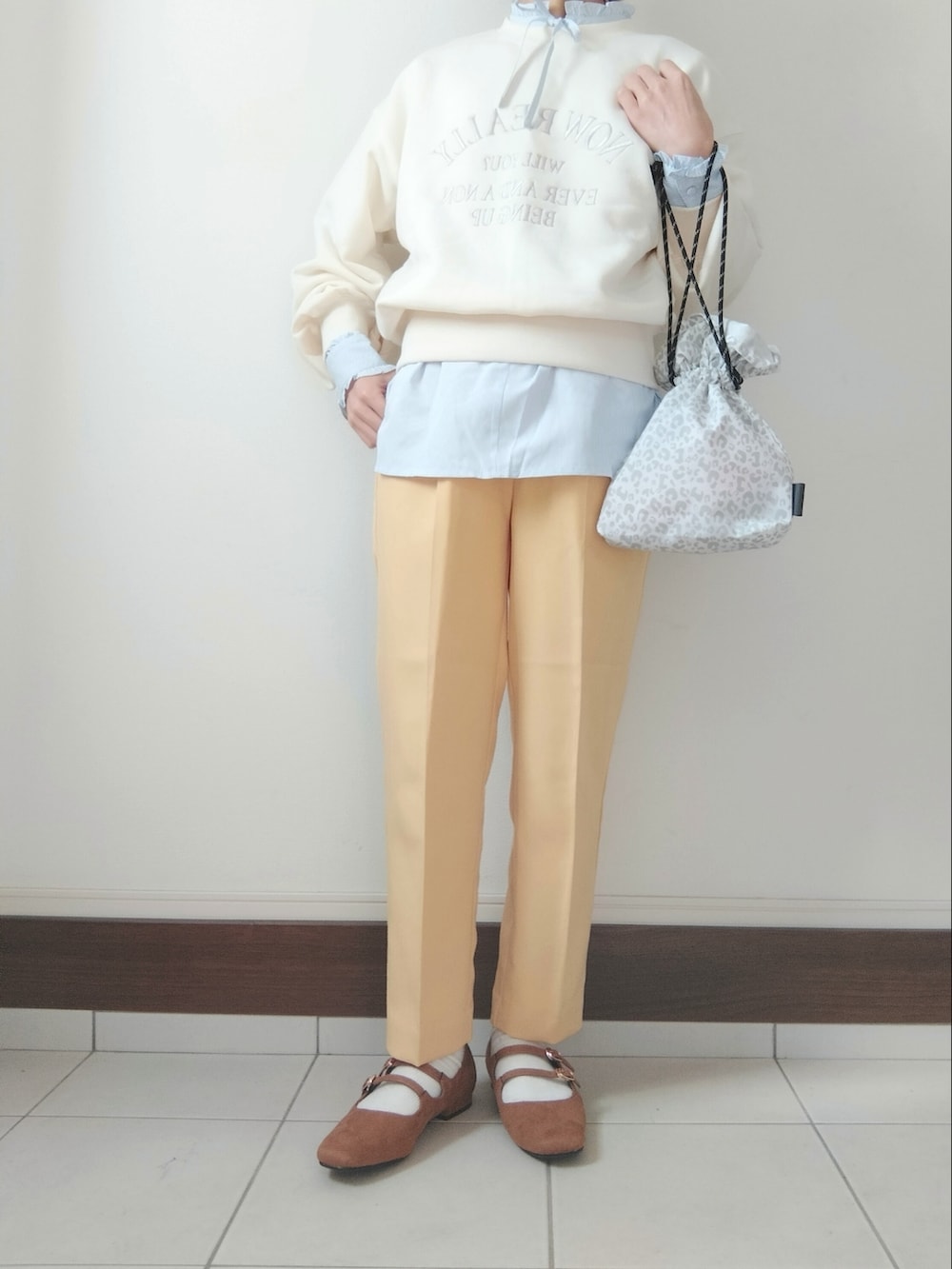ホワイト系のスウェット、イエロー系のスラックス、ホワイト系のショルダーバッグを着用したレディースの冬コーディネートの2枚目の写真
