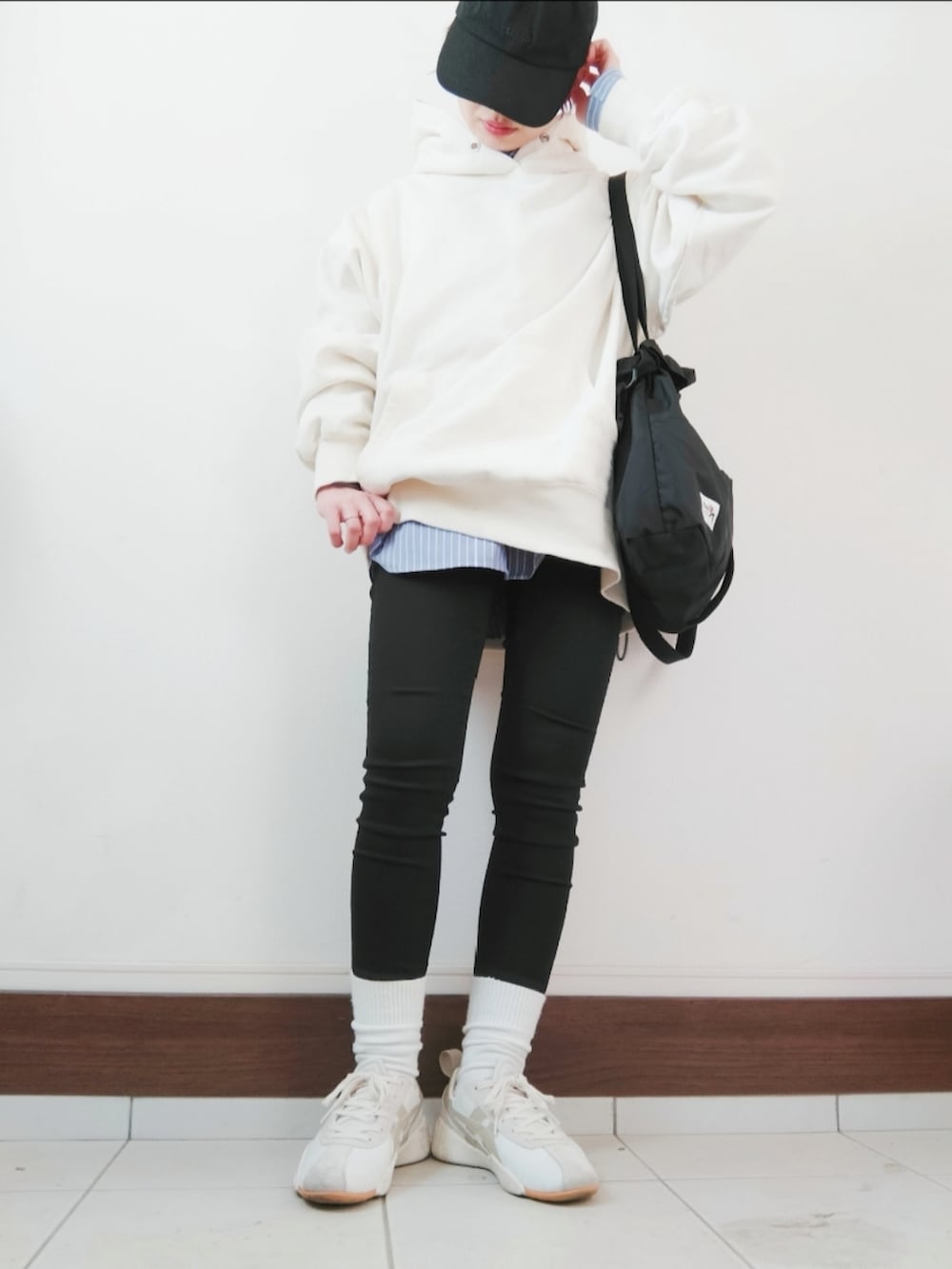 ホワイト系のパーカー、ブラック系のショルダーバッグ、ブラック系のデニムパンツを着用したレディースの冬コーディネートの2枚目の写真