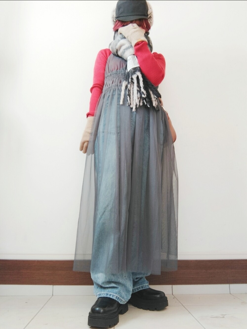 グレー系のワンピース、ブラック系のブーツ、ブルー系のデニムパンツを着用したレディースの冬コーディネートの2枚目の写真