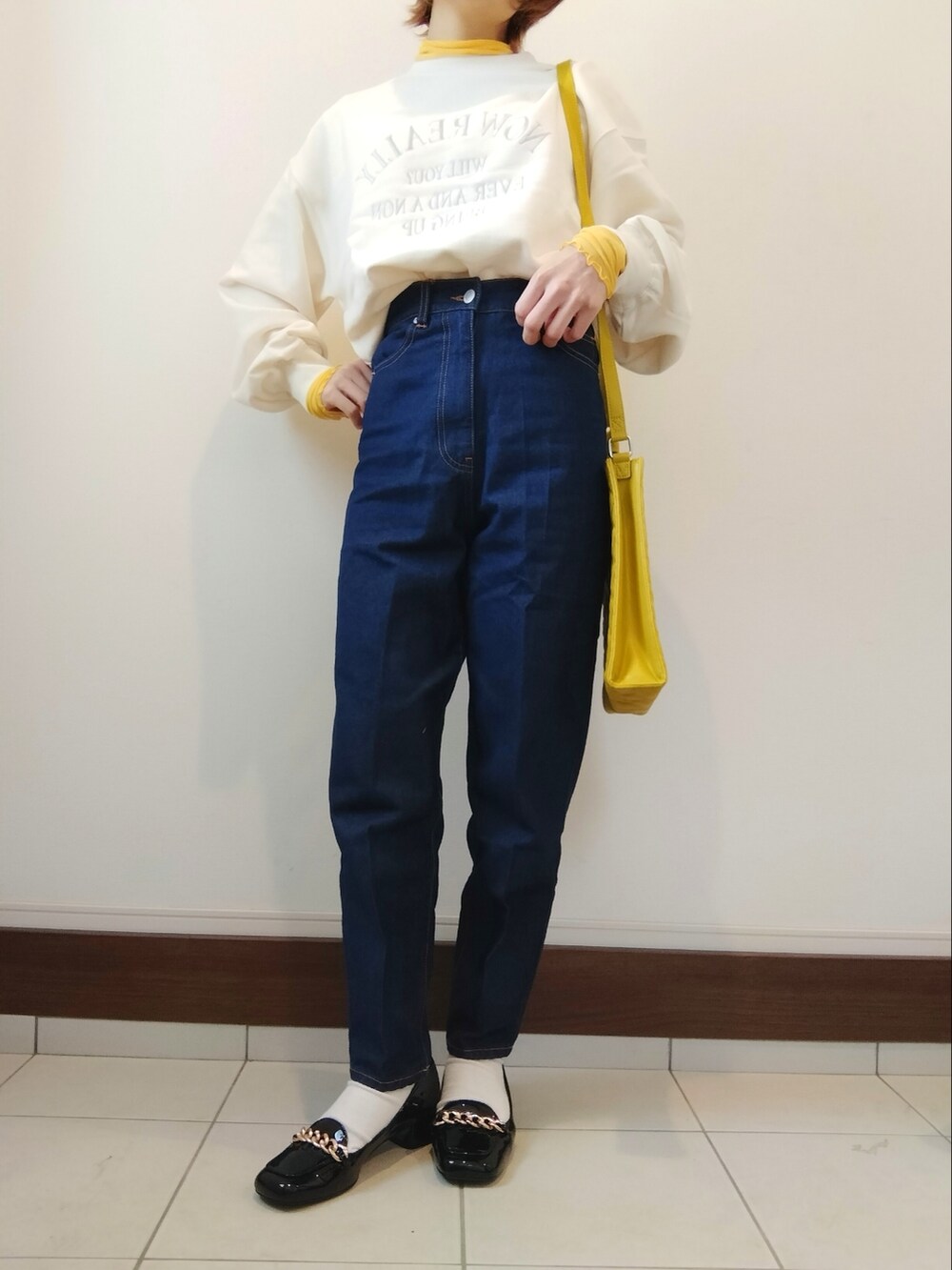 ホワイト系のスウェット、イエロー系のショルダーバッグ、ブルー系のデニムパンツを着用したレディースの冬コーディネートの2枚目の写真