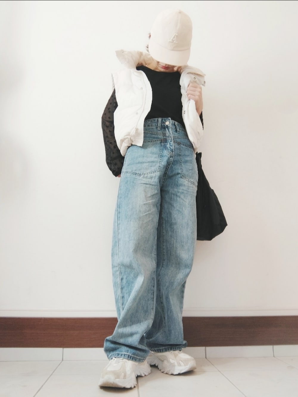 ホワイト系のダウンベスト、ブラック系のショルダーバッグ、ブルー系のデニムパンツを着用したレディースの秋コーディネートの2枚目の写真