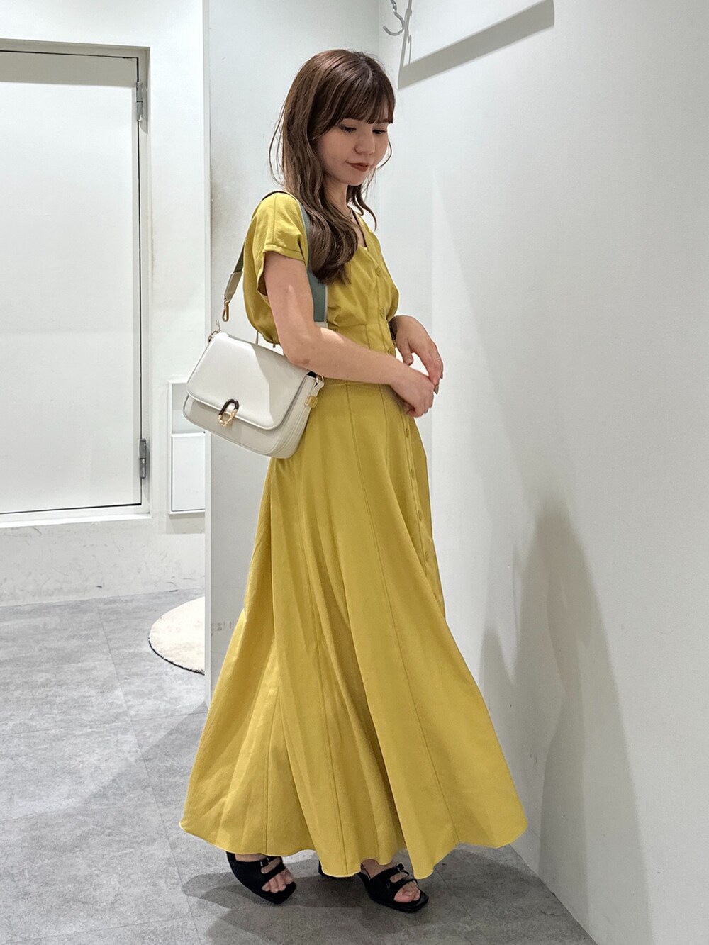 イエロー系のワンピース、ブラック系のサンダル、ホワイト系のショルダーバッグを着用したレディースの夏コーディネートの2枚目の写真