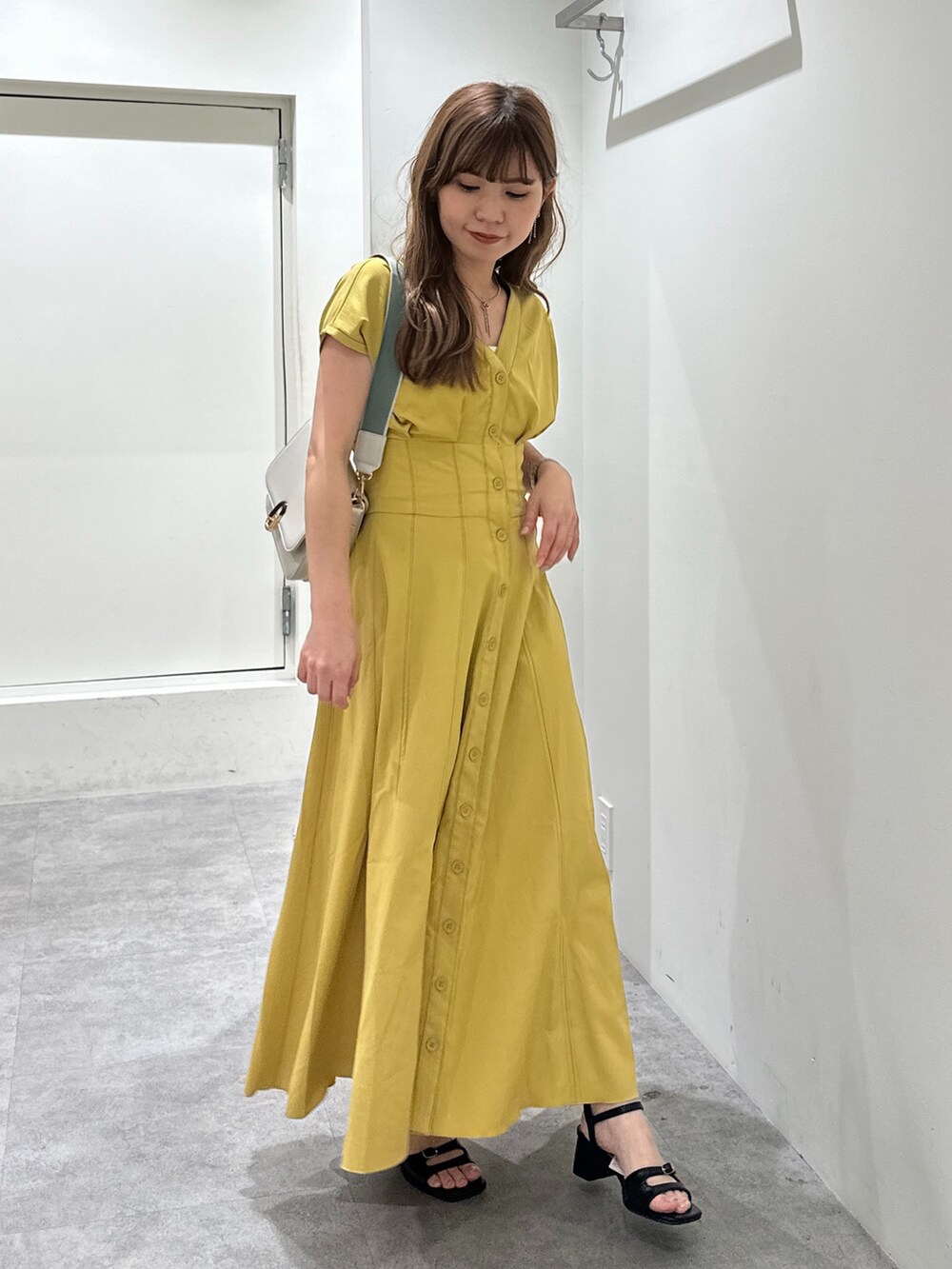 イエロー系のワンピース、ブラック系のサンダル、ホワイト系のショルダーバッグを着用したレディースの夏コーディネートの4枚目の写真