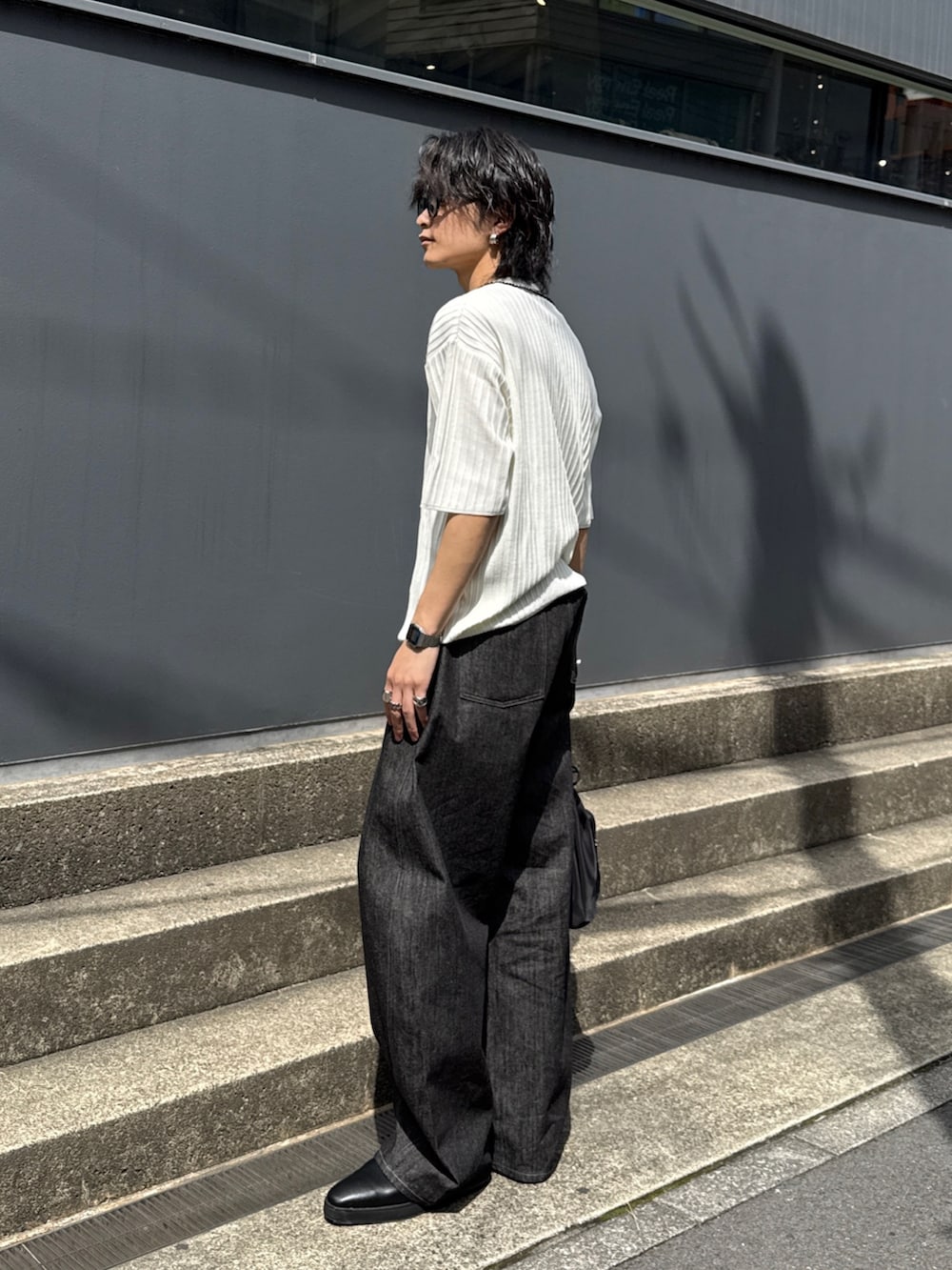 ブラック系のデニムパンツ、ブラック系のショルダーバッグ、ホワイト系のニット/セーターを着用したメンズの春コーディネートの2枚目の写真