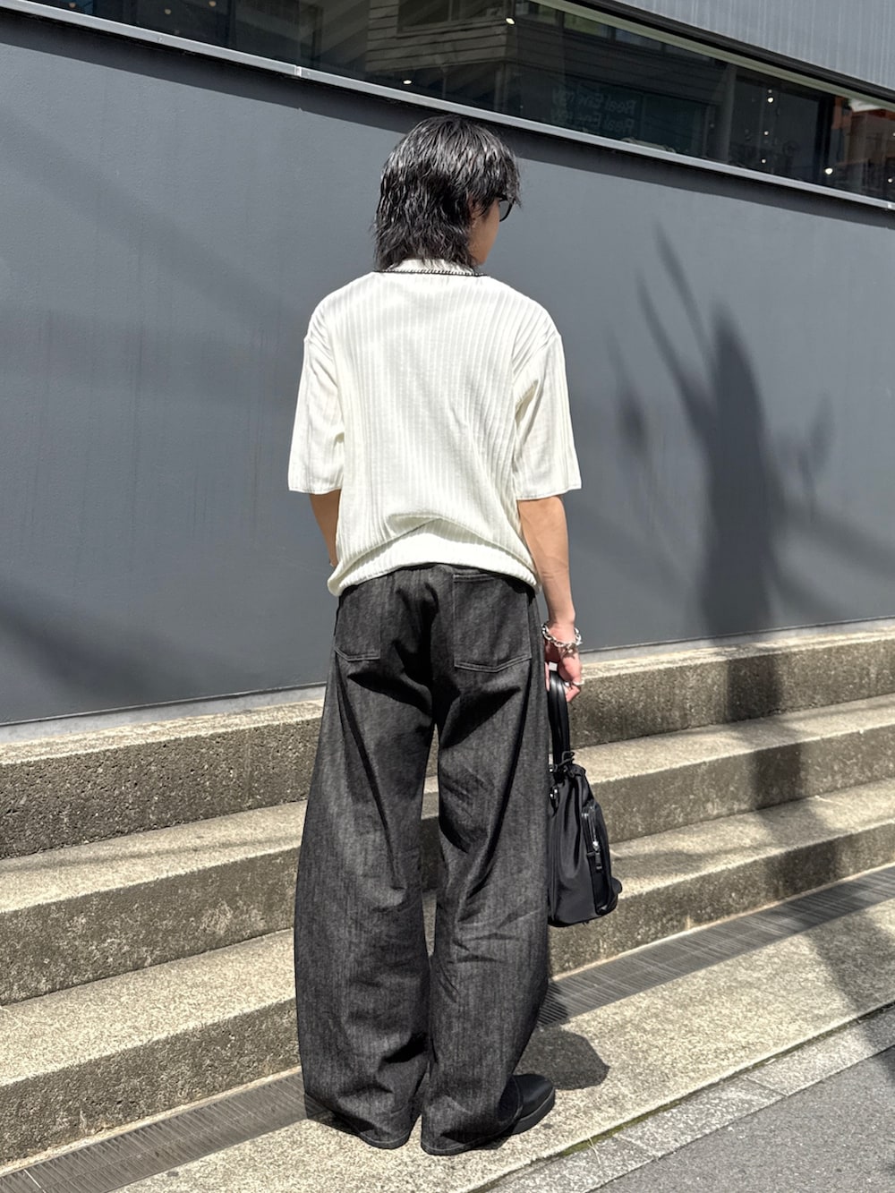 ブラック系のデニムパンツ、ブラック系のショルダーバッグ、ホワイト系のニット/セーターを着用したメンズの春コーディネートの3枚目の写真