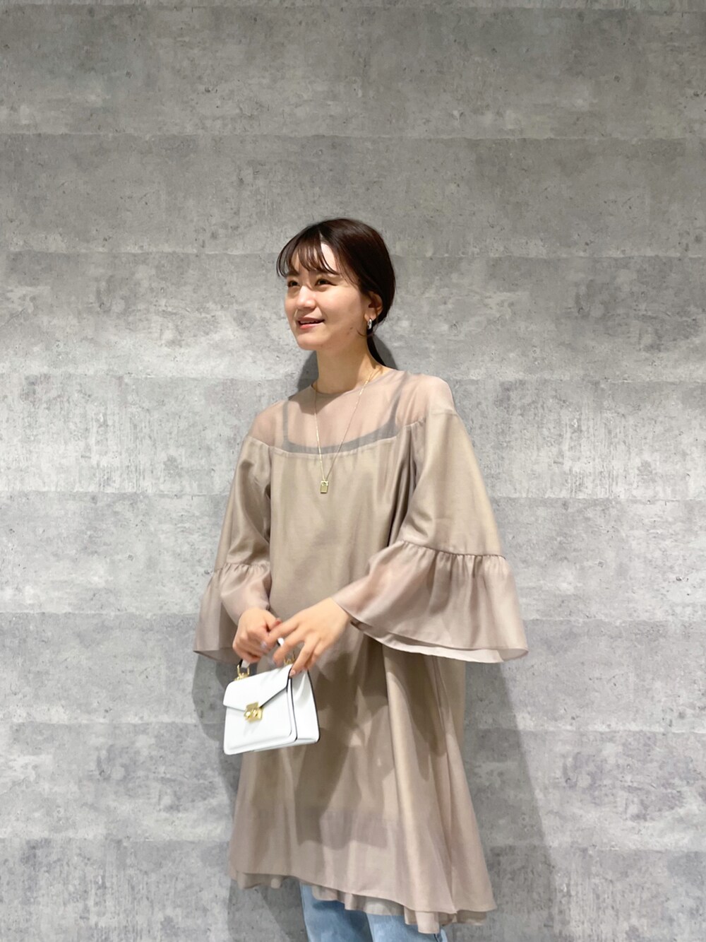 ベージュ系のワンピース、ホワイト系のバッグ、ブルー系のデニムパンツを着用したレディースの春コーディネートの3枚目の写真