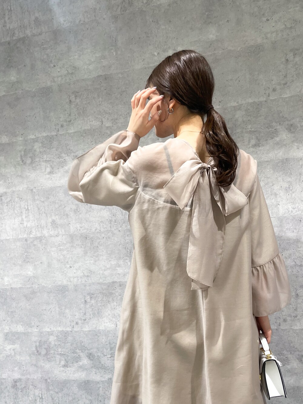 ベージュ系のワンピース、ホワイト系のバッグ、ブルー系のデニムパンツを着用したレディースの春コーディネートの2枚目の写真