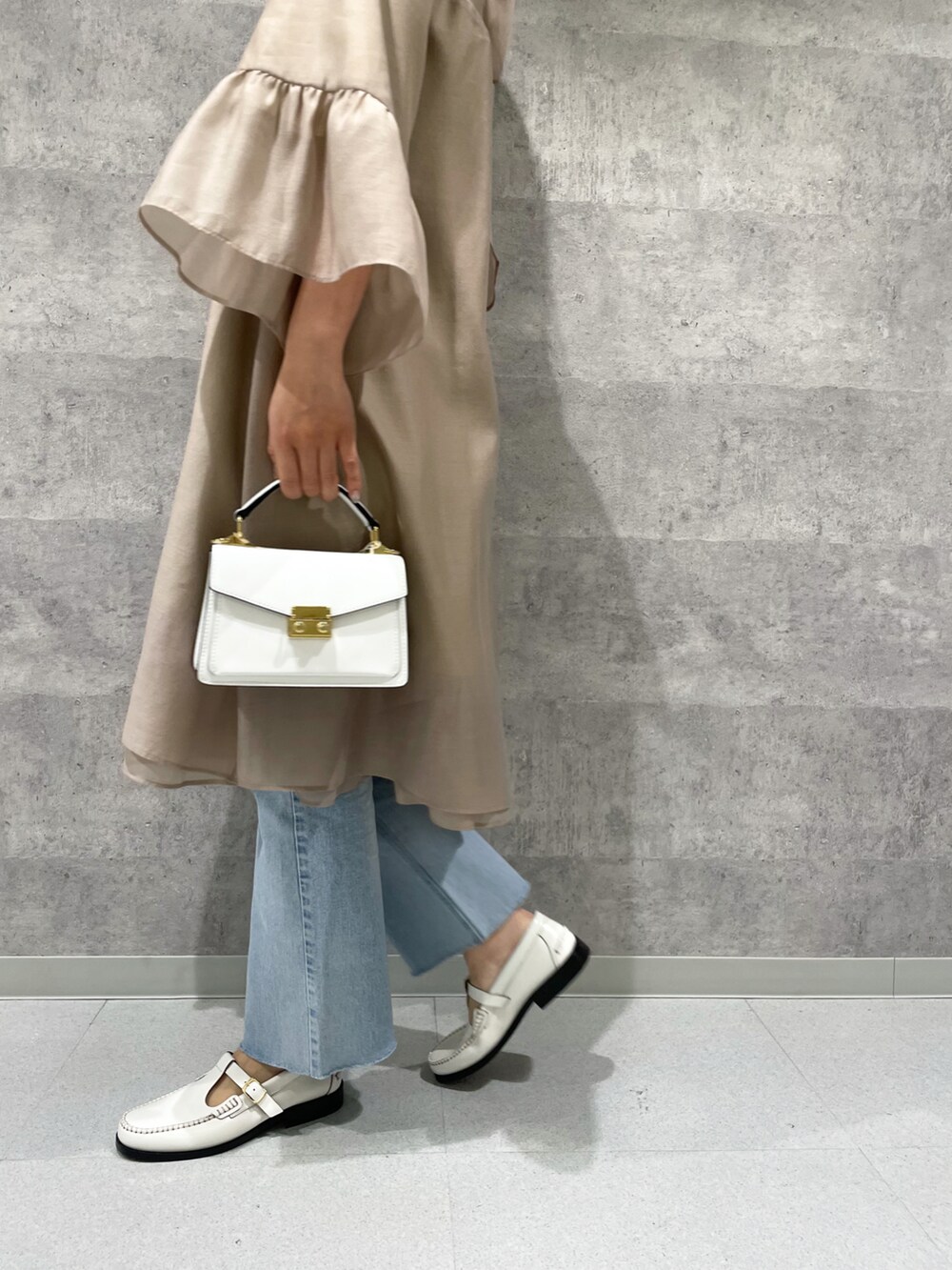 ベージュ系のワンピース、ホワイト系のバッグ、ブルー系のデニムパンツを着用したレディースの春コーディネートの4枚目の写真