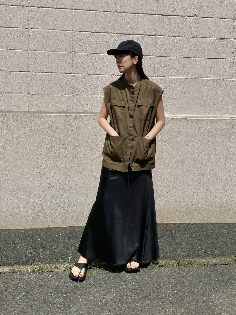 グリーン系のベスト、ブラック系のスカート、ブラック系のサンダルを着用したレディースの夏コーディネートの2枚目の写真