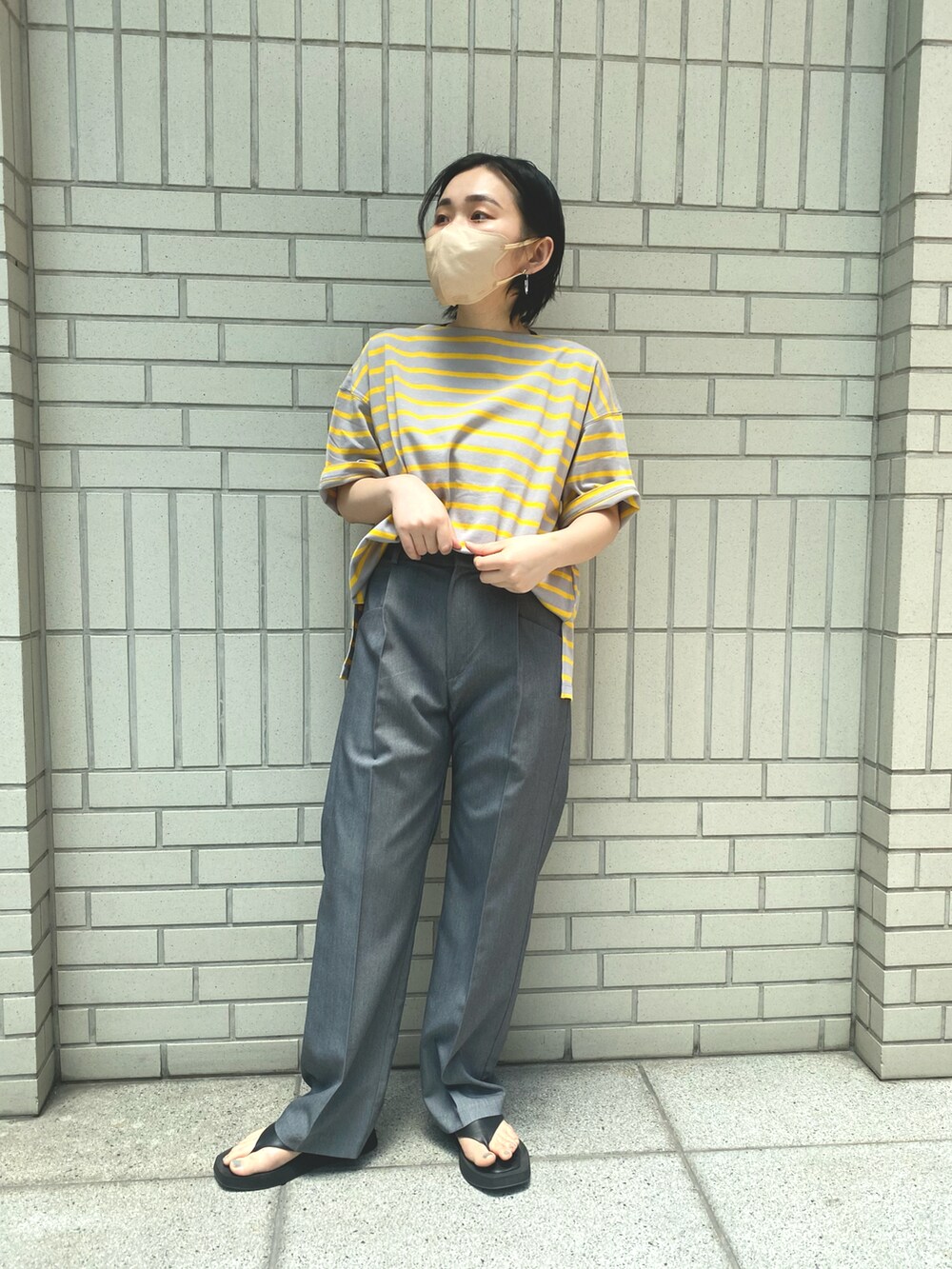 グレー系のスラックス、イエロー系のTシャツ/カットソー、ブラック系のサンダルを着用したレディースの夏コーディネートの3枚目の写真