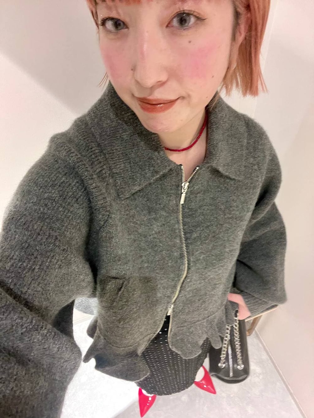 レッド系のパンプス、ブラック系のショルダーバッグ、ブラック系のスカートを着用したレディースの冬コーディネートの3枚目の写真