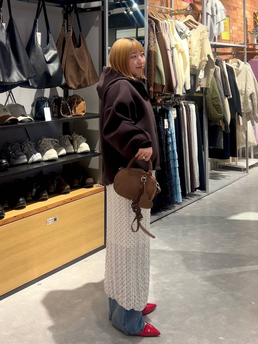 レッド系のパンプス、ブラウン系のボストンバッグ、ブルー系のデニムパンツを着用したレディースの春コーディネートの2枚目の写真