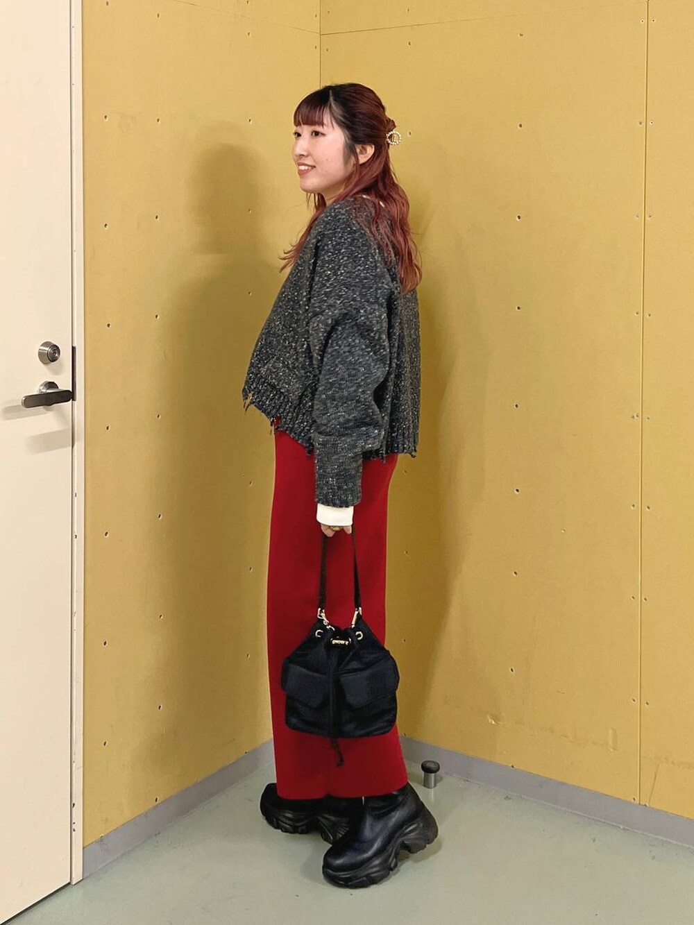 レッド系のスカート、ブラック系のショルダーバッグ、ブラック系のブーツを着用したレディースの秋コーディネートの2枚目の写真