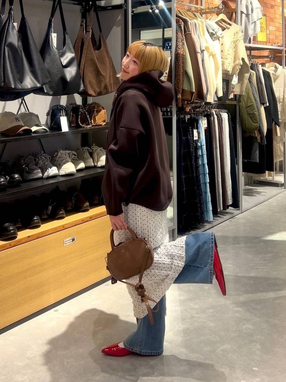 レッド系のパンプス、ブラウン系のボストンバッグ、ブルー系のデニムパンツを着用したレディースの春コーディネートの3枚目の写真