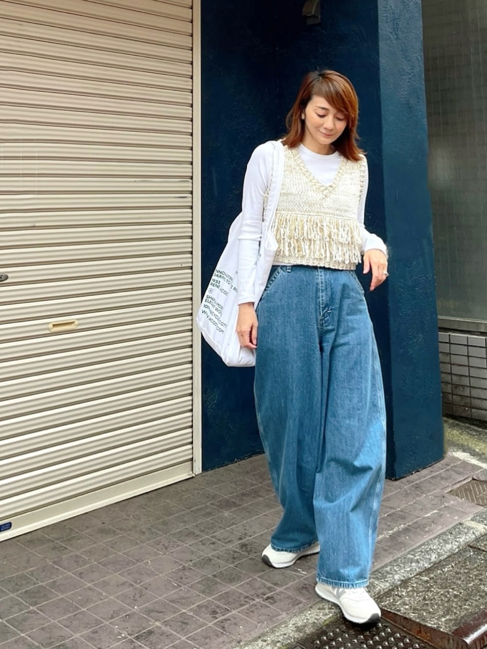 ホワイト系のベスト、ブルー系のデニムパンツ、ホワイト系のスニーカーを着用したレディースの春コーディネートの3枚目の写真