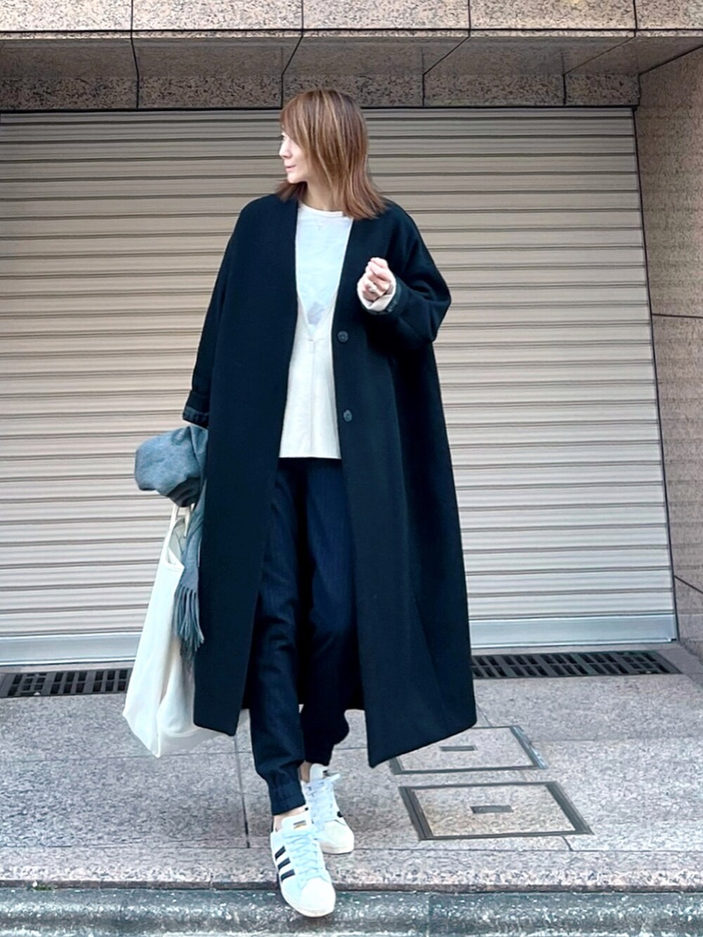 ホワイト系のスニーカー、ブラック系のノーカラーコート、ベージュ系のTシャツ/カットソーを着用したレディースの冬コーディネートの2枚目の写真