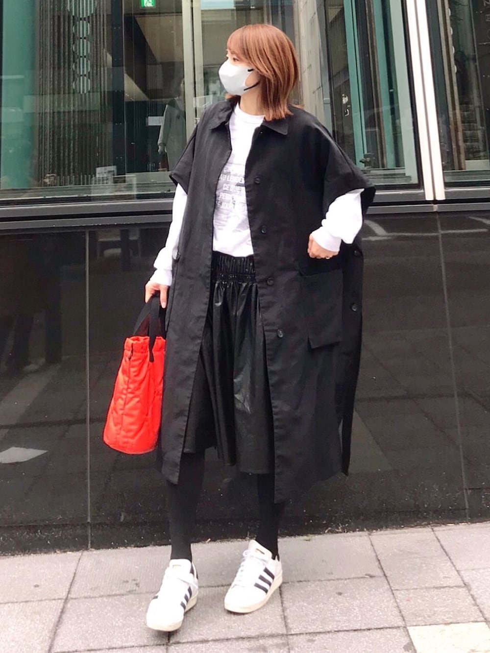 オレンジ系のトートバッグ、ブラック系のステンカラーコート、ホワイト系のTシャツ/カットソーを着用したレディースの春コーディネートの2枚目の写真