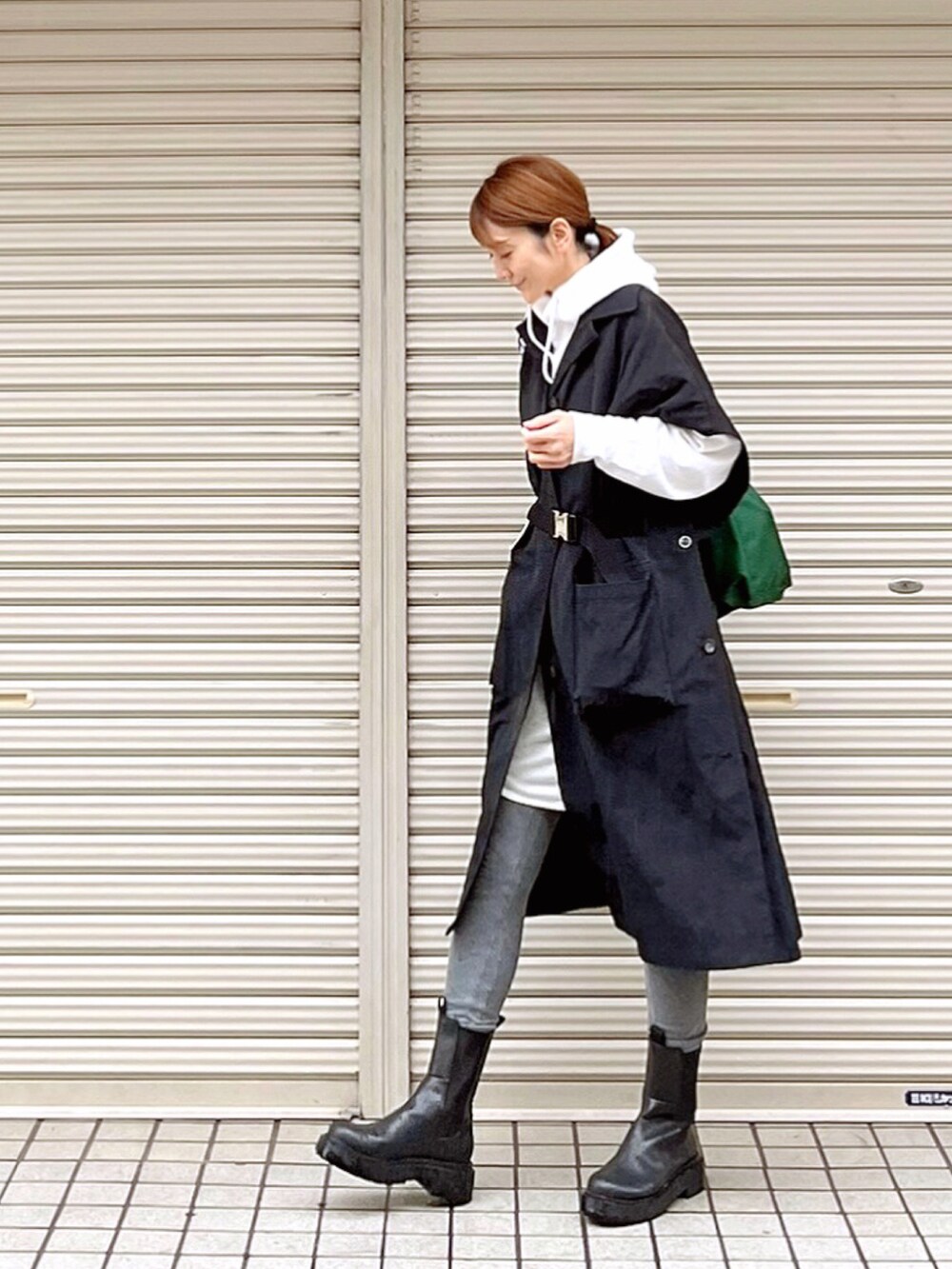 ブラック系のステンカラーコート、ブラック系のブーツ、ホワイト系のTシャツ/カットソーを着用したレディースの秋コーディネートの4枚目の写真