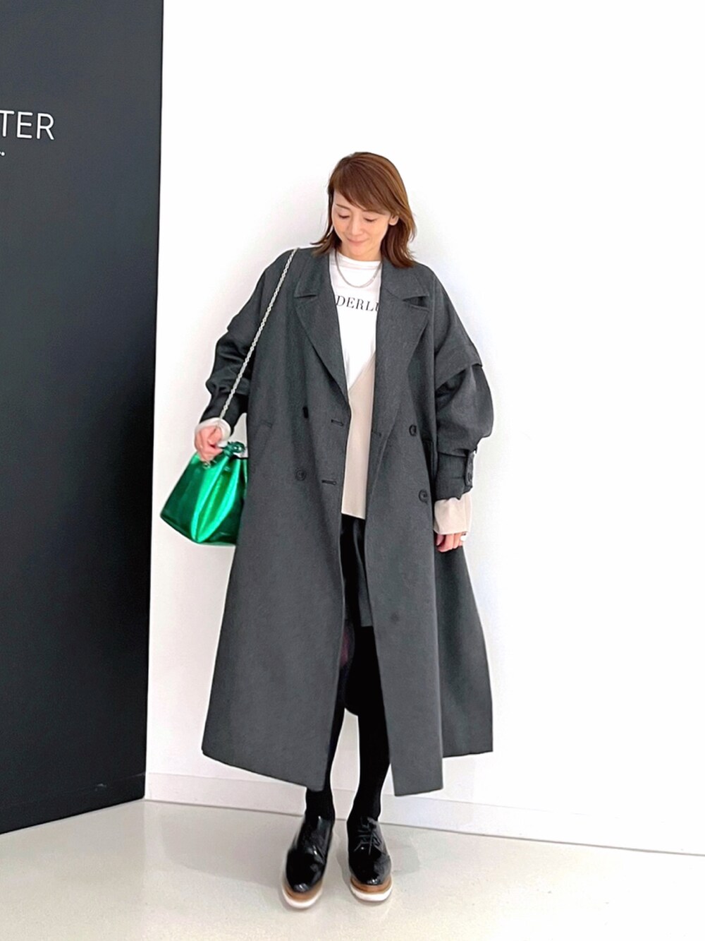 グレー系のチェスターコート、グリーン系のショルダーバッグ、ブラック系のその他パンツを着用したレディースの春コーディネートの2枚目の写真