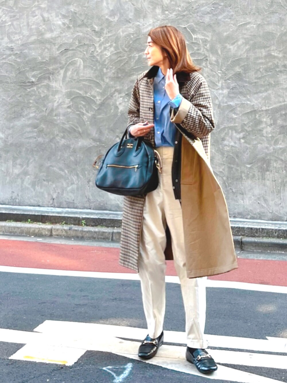 ブラック系のローファー、ベージュ系のステンカラーコート、ブラック系のショルダーバッグを着用したレディースの冬コーディネートの2枚目の写真