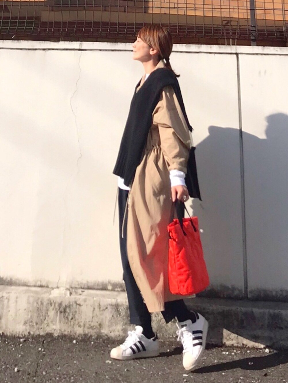 オレンジ系のトートバッグ、ブラック系のニット/セーター、ベージュ系のワンピースを着用したレディースの春コーディネートの3枚目の写真