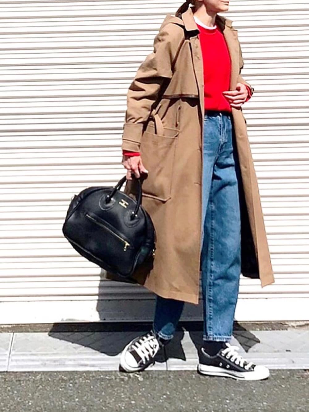 レッド系のニット/セーター、ベージュ系のトレンチコート、ブルー系のデニムパンツを着用したレディースの春コーディネートの2枚目の写真