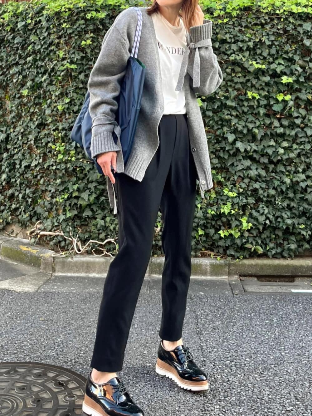 グリーン系のトートバッグ、ホワイト系のTシャツ/カットソー、グレー系のニット/セーターを着用したレディースの秋コーディネートの2枚目の写真