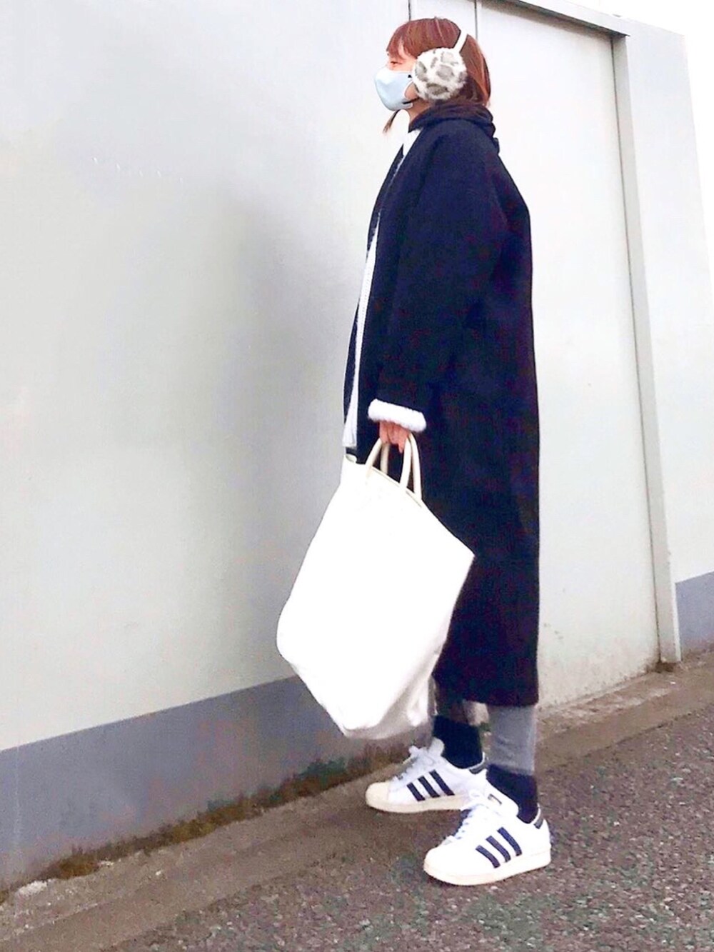 ブラック系のノーカラーコート、ホワイト系のスニーカー、ホワイト系のトートバッグを着用したレディースの冬コーディネートの2枚目の写真