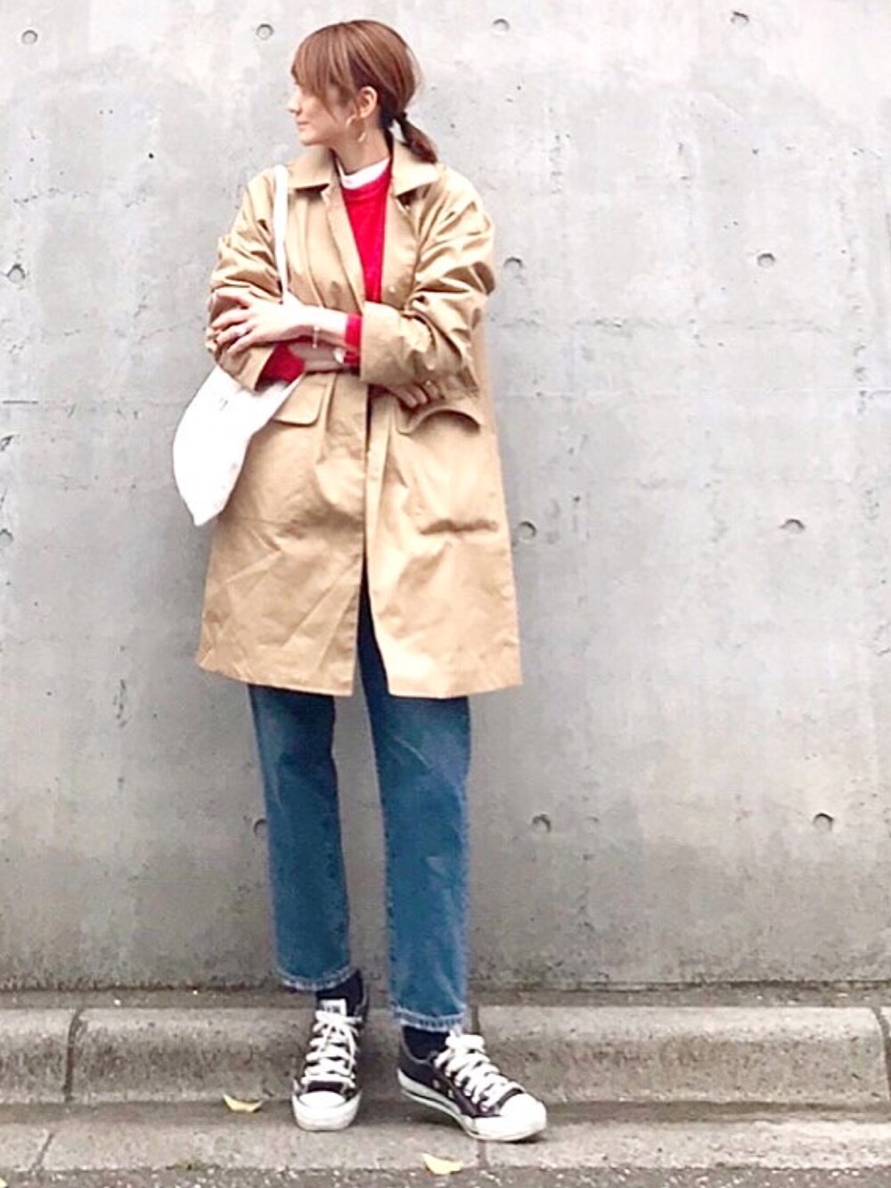 レッド系のニット/セーター、ベージュ系のステンカラーコート、ブルー系のデニムパンツを着用したレディースの春コーディネートの3枚目の写真