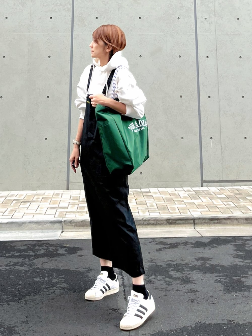グリーン系のトートバッグ、ホワイト系のパーカー、ブラック系のスカートを着用したレディースの秋コーディネートの4枚目の写真
