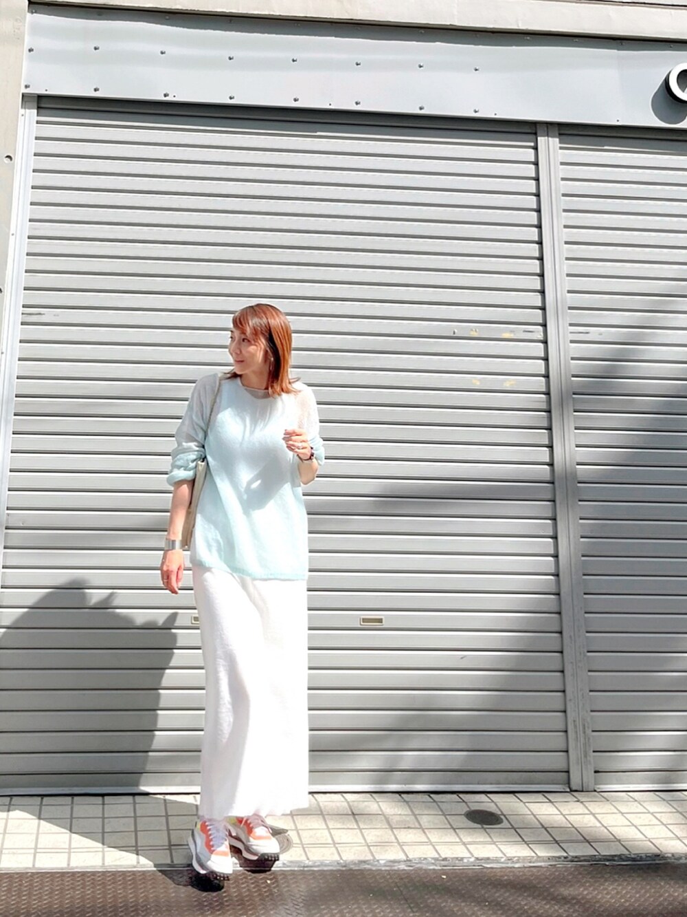 グレー系のスニーカー、ブルー系のニット/セーター、ホワイト系のワンピースを着用したレディースの秋コーディネートの2枚目の写真