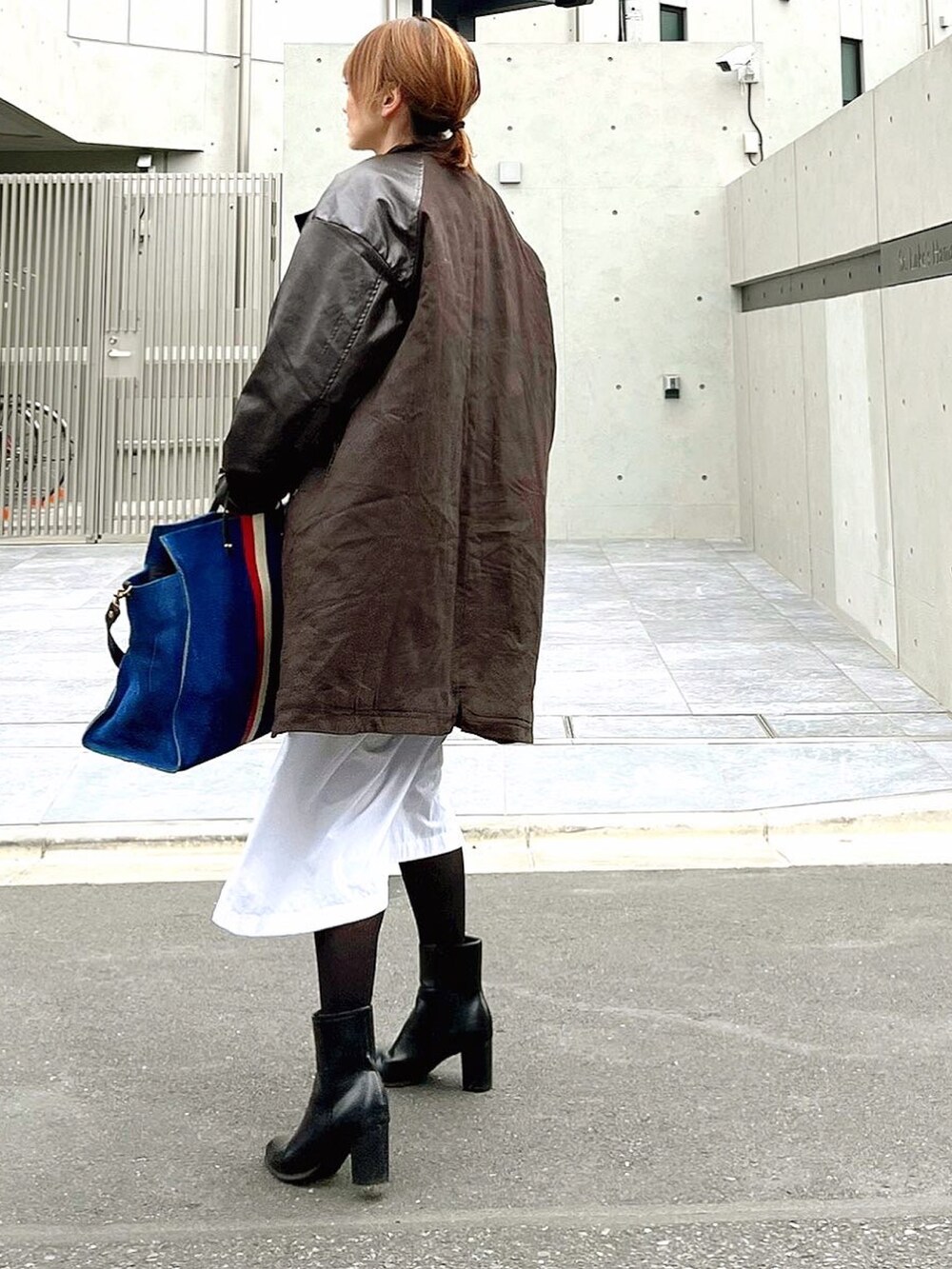 ブラウン系のミリタリージャケット、ブルー系のトートバッグ、ホワイト系のシャツワンピースを着用したレディースの冬コーディネートの2枚目の写真