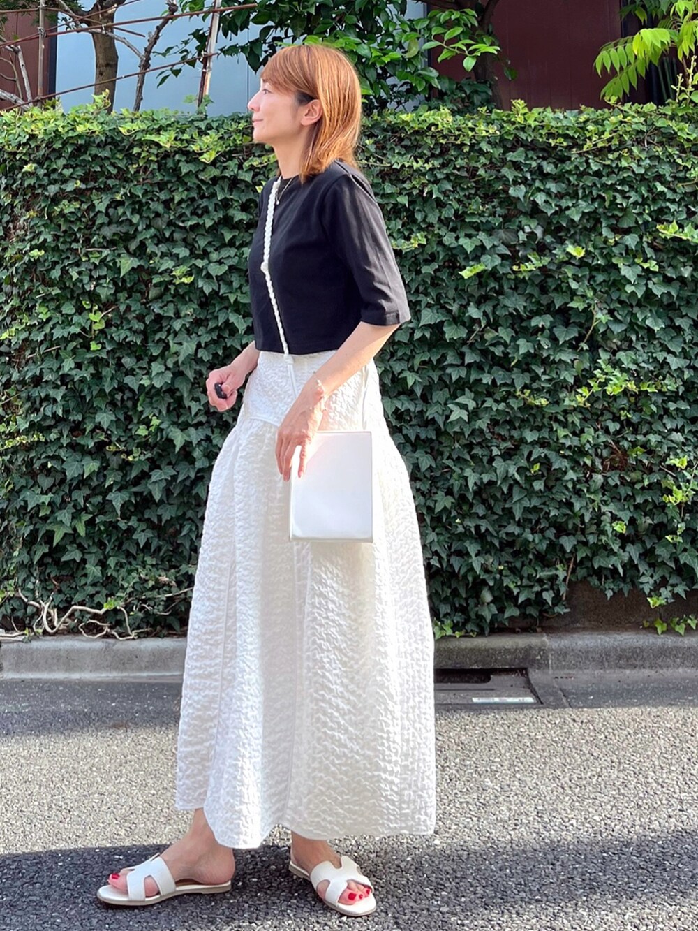 ブラック系のTシャツ/カットソー、ホワイト系のスカート、ホワイト系のサンダルを着用したレディースの夏コーディネートの2枚目の写真