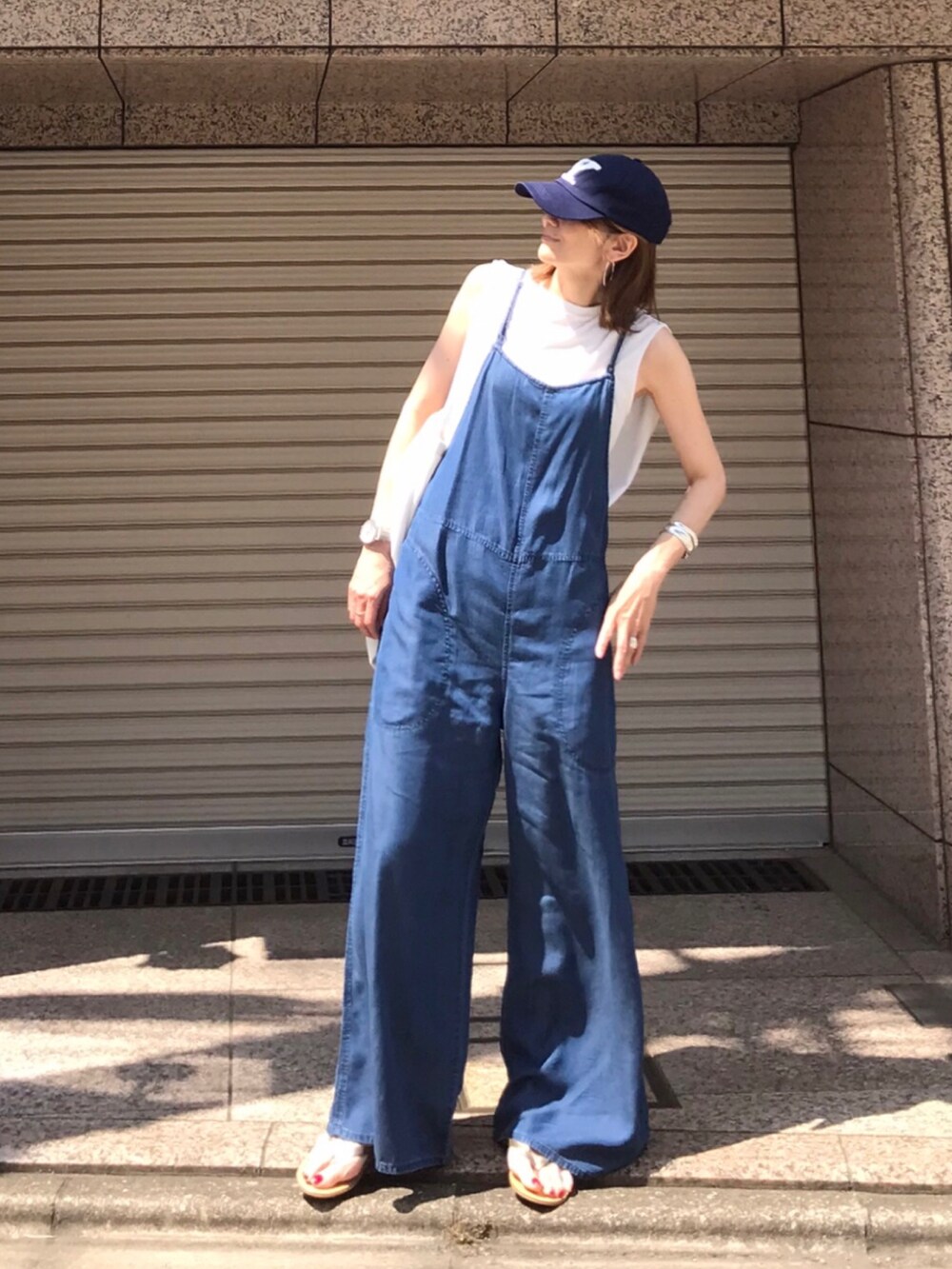 ホワイト系のトートバッグ、ブルー系のサロペット/オーバーオール、ゴールド系のサンダルを着用したレディースの夏コーディネートの2枚目の写真