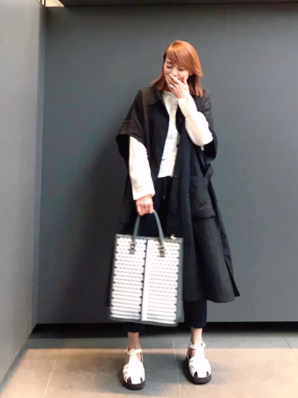 ブラック系のステンカラーコート、ブラック系のトートバッグ、ホワイト系のサンダルを着用したレディースの春コーディネートの2枚目の写真
