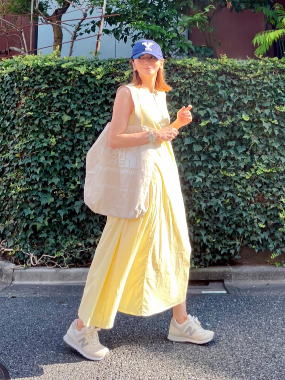 イエロー系のワンピース、ホワイト系のトートバッグ、ホワイト系のスニーカーを着用したレディースの夏コーディネートの2枚目の写真
