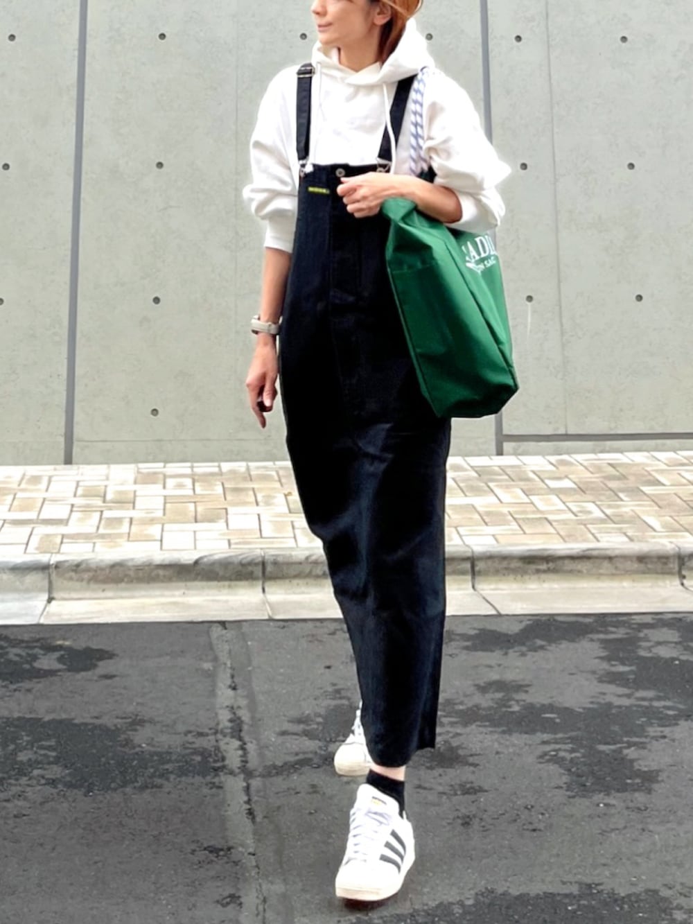 グリーン系のトートバッグ、ホワイト系のパーカー、ブラック系のスカートを着用したレディースの秋コーディネートの2枚目の写真